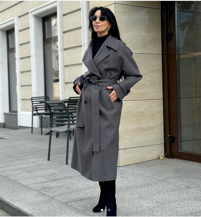 Жінка-модель на показі моди одягнена у пальто сірого кольору із хутровим коміром.